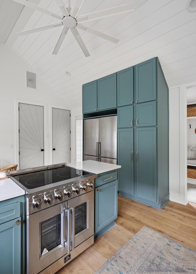 kitchen with vaulted ceiling, blue cabinets, ceiling fan, stainless steel appliances, and light wood-type flooring