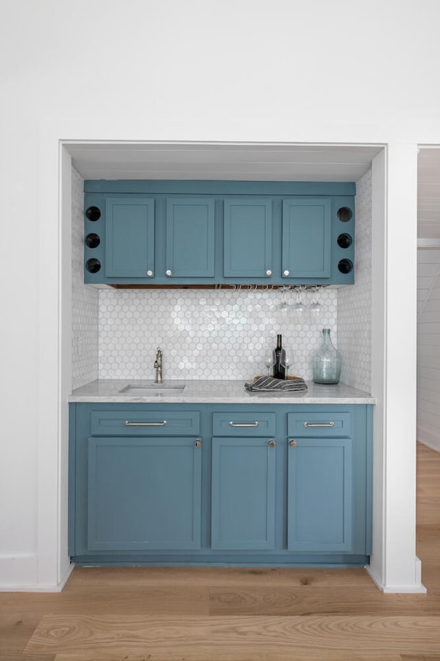 bar with blue cabinetry, sink, and light wood-type flooring