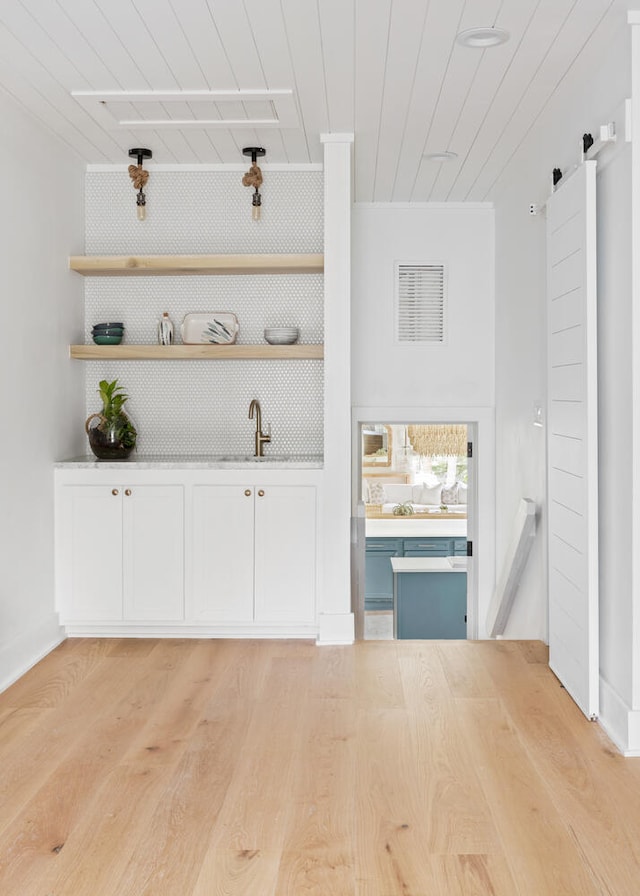 bar with sink, light hardwood / wood-style flooring, white cabinets, wooden ceiling, and a barn door