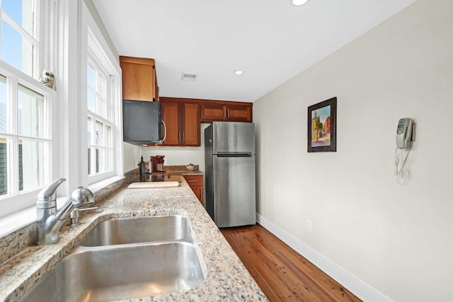 kitchen featuring stainless steel refrigerator, dark hardwood / wood-style floors, sink, and light stone counters