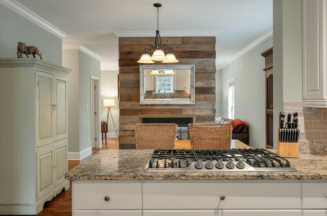 kitchen with a fireplace, stainless steel gas cooktop, light stone countertops, ornamental molding, and a chandelier