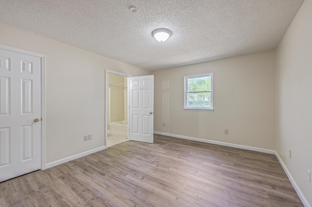 unfurnished bedroom with connected bathroom, baseboards, a textured ceiling, and wood finished floors