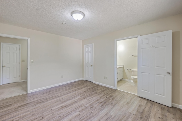 unfurnished bedroom with a textured ceiling, baseboards, light wood-type flooring, and connected bathroom