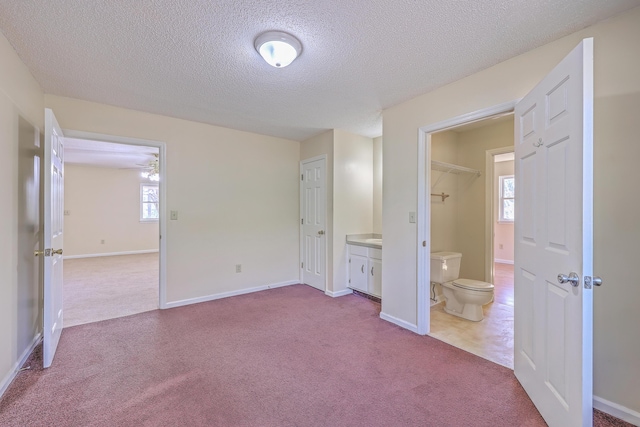 unfurnished bedroom with ensuite bath, baseboards, dark carpet, and a textured ceiling