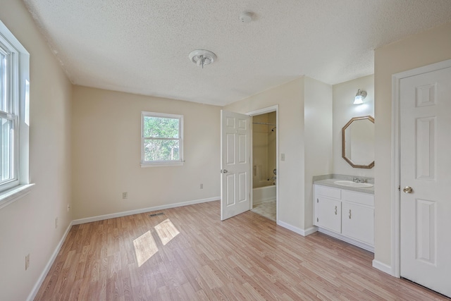 unfurnished bedroom featuring a sink, connected bathroom, baseboards, and light wood finished floors