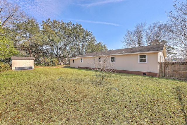 back of house featuring fence, a lawn, an outdoor structure, crawl space, and a storage unit