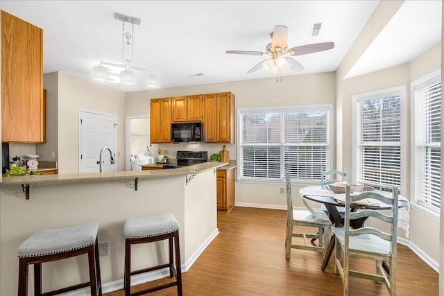 kitchen with kitchen peninsula, stainless steel electric stove, hanging light fixtures, light hardwood / wood-style floors, and a breakfast bar area