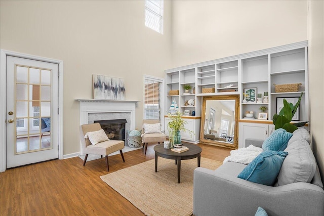 living area featuring a premium fireplace, a towering ceiling, a healthy amount of sunlight, and hardwood / wood-style floors