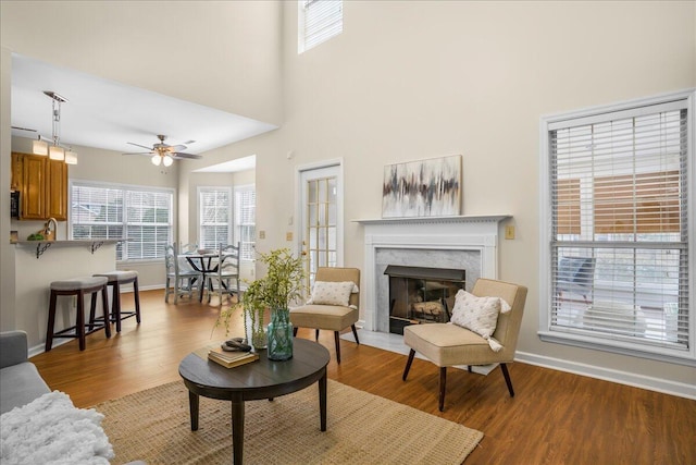 living room featuring light hardwood / wood-style floors, ceiling fan, a towering ceiling, and a premium fireplace