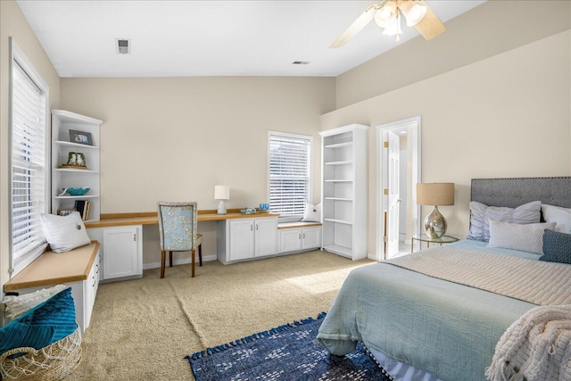 bedroom featuring vaulted ceiling, light carpet, built in desk, ceiling fan, and multiple windows