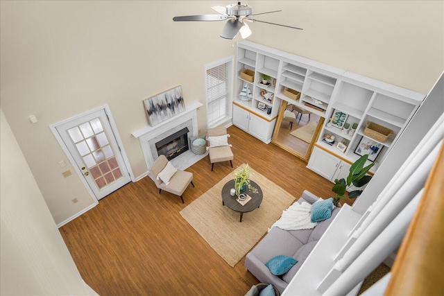 living room with built in shelves, light wood-type flooring, a towering ceiling, and ceiling fan