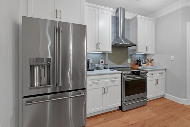 kitchen featuring wall chimney range hood, light hardwood / wood-style floors, backsplash, appliances with stainless steel finishes, and white cabinetry