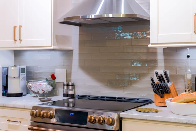 kitchen with wall chimney range hood, stainless steel range, decorative backsplash, and white cabinets