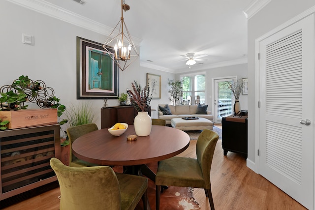 dining space featuring ceiling fan with notable chandelier, beverage cooler, light hardwood / wood-style floors, and ornamental molding