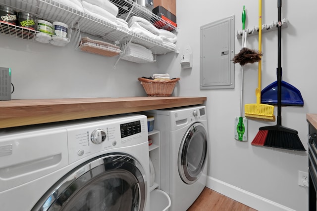 laundry room with electric panel, washer and dryer, and light wood-type flooring