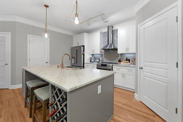 kitchen featuring white cabinets, hanging light fixtures, a center island with sink, wall chimney range hood, and appliances with stainless steel finishes