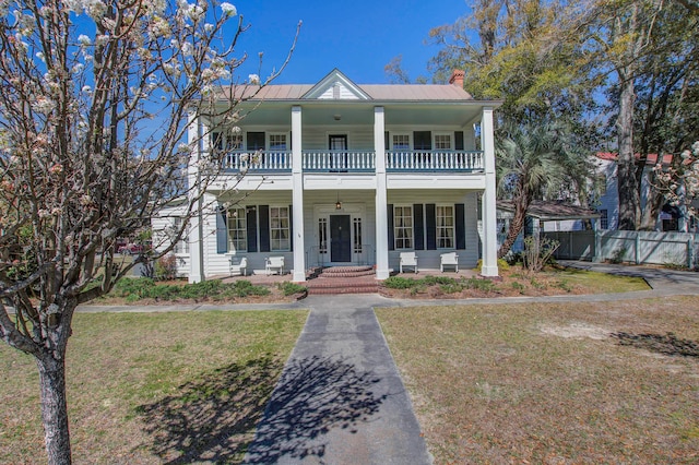 greek revival inspired property with a front lawn, a balcony, and a porch