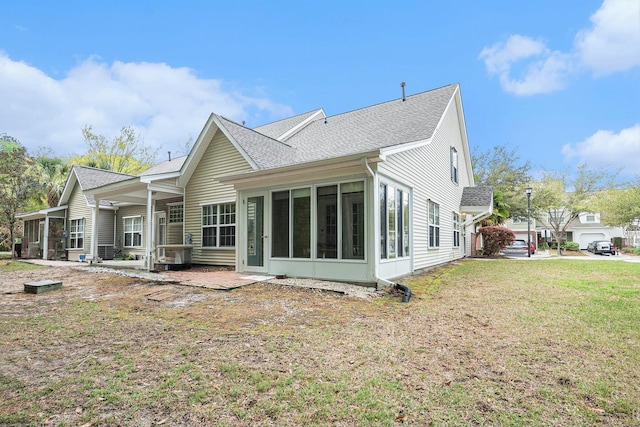 rear view of house featuring a sunroom, roof with shingles, and a lawn