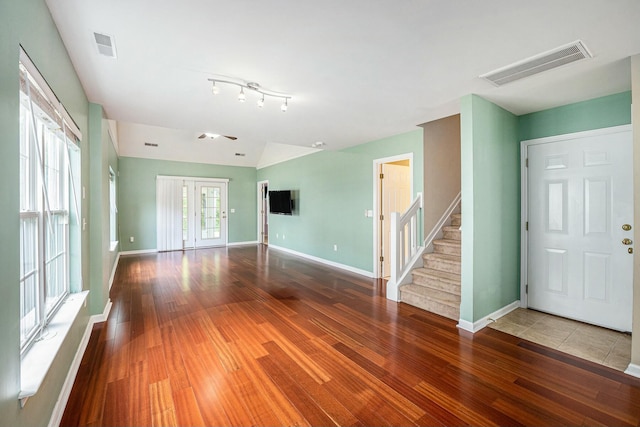 unfurnished living room with wood finished floors, baseboards, visible vents, and stairway