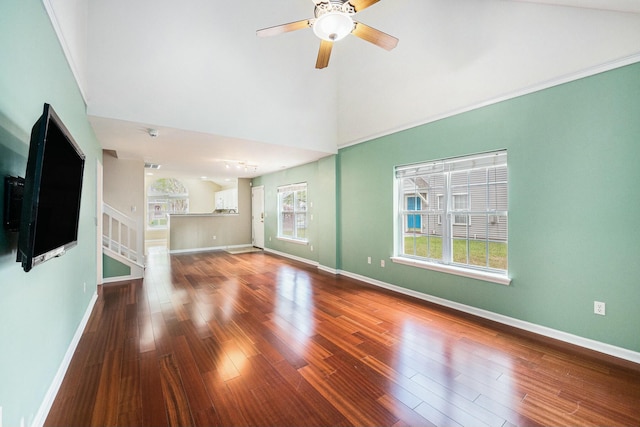 unfurnished living room with ceiling fan, a towering ceiling, wood finished floors, stairs, and baseboards