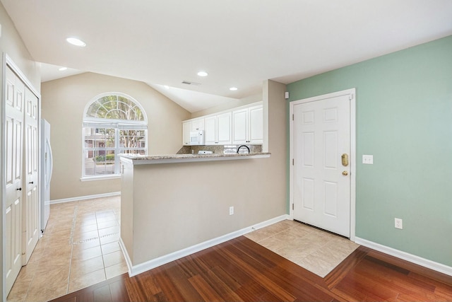 kitchen with visible vents, light wood-type flooring, white microwave, white cabinetry, and vaulted ceiling