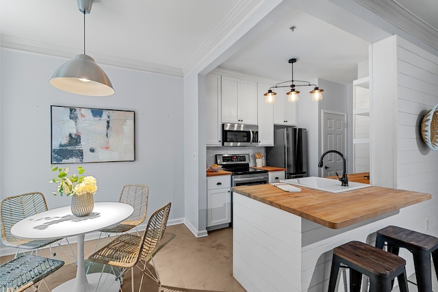 kitchen with a kitchen island with sink, white cabinets, hanging light fixtures, butcher block countertops, and stainless steel appliances