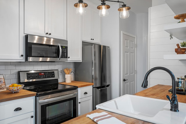 kitchen featuring butcher block counters, sink, hanging light fixtures, white cabinetry, and stainless steel appliances