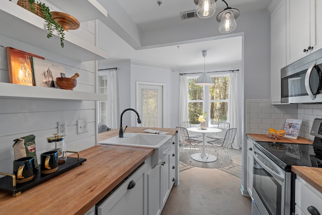 kitchen with pendant lighting, butcher block counters, tasteful backsplash, white cabinetry, and stainless steel appliances