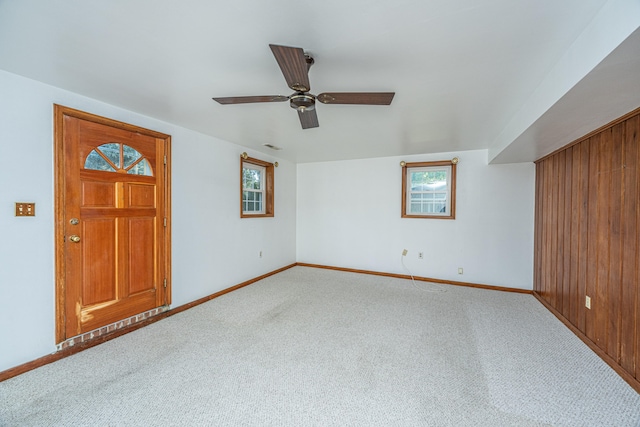 interior space featuring a healthy amount of sunlight, wooden walls, carpet flooring, and ceiling fan