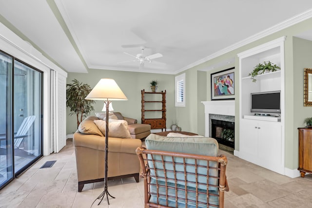 living area with built in shelves, visible vents, a fireplace, ceiling fan, and ornamental molding