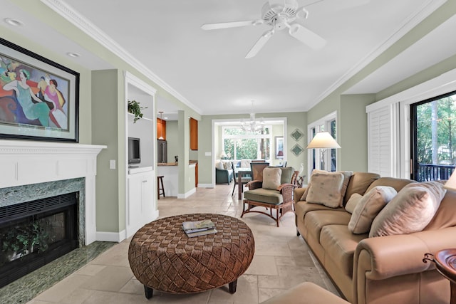 living area featuring ornamental molding, ceiling fan with notable chandelier, stone tile flooring, a high end fireplace, and baseboards