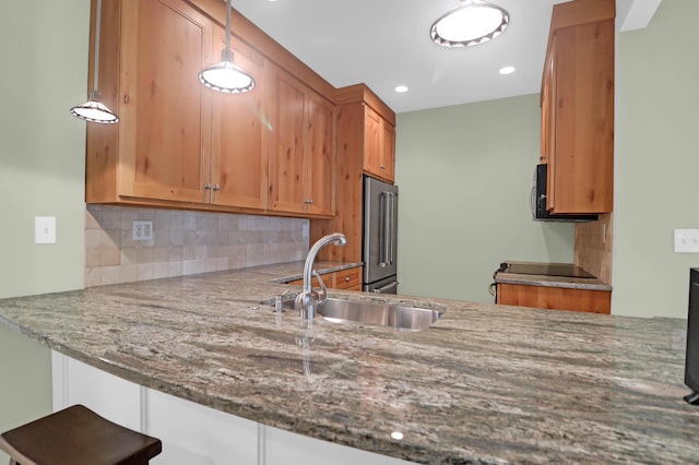 kitchen featuring brown cabinetry, stone counters, a sink, decorative backsplash, and high end refrigerator