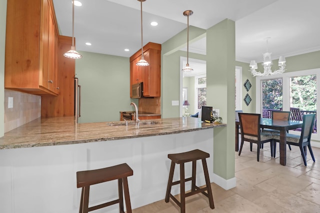 kitchen with brown cabinetry, stainless steel microwave, a peninsula, and a sink