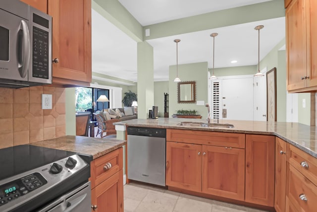 kitchen featuring open floor plan, light stone counters, decorative backsplash, stainless steel appliances, and a sink