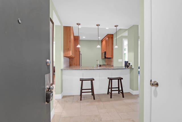 kitchen with a sink, stainless steel microwave, a kitchen breakfast bar, stone counters, and baseboards