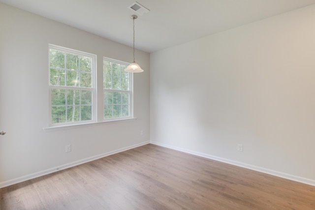 spare room with wood finished floors, visible vents, and baseboards