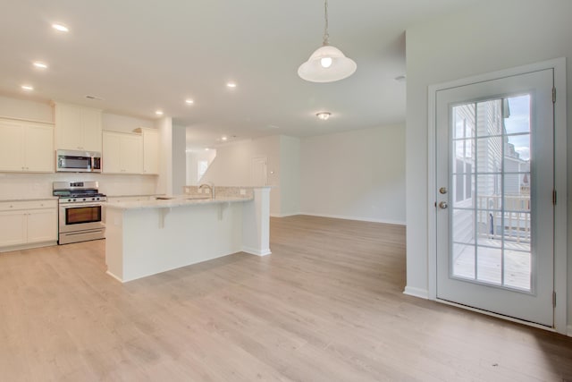 kitchen with light stone counters, stainless steel appliances, light wood-style floors, open floor plan, and a kitchen bar