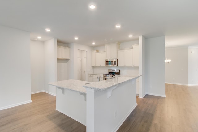 kitchen with light wood finished floors, white cabinetry, appliances with stainless steel finishes, and light stone counters