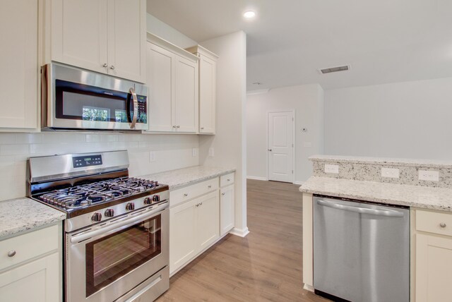 kitchen with visible vents, decorative backsplash, appliances with stainless steel finishes, light stone counters, and light wood-type flooring