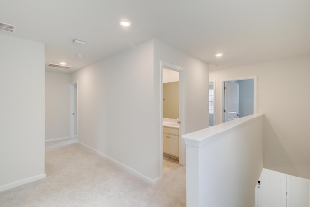 hall with baseboards, visible vents, light colored carpet, and an upstairs landing