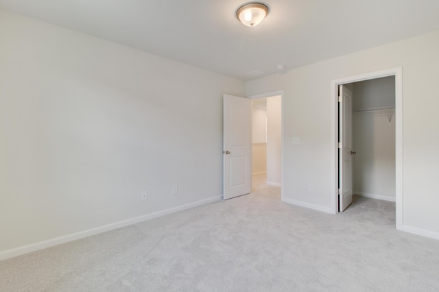 unfurnished bedroom featuring baseboards, a closet, a walk in closet, and light colored carpet