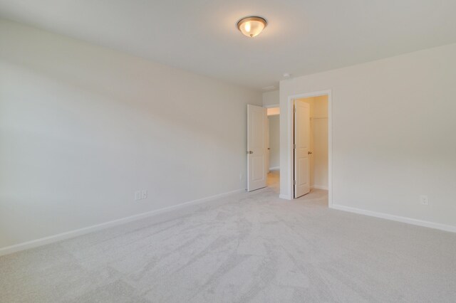 unfurnished bedroom featuring light carpet, a spacious closet, a closet, and baseboards