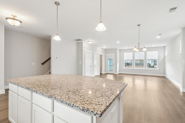 kitchen featuring hardwood / wood-style floors, decorative light fixtures, light stone counters, and white cabinetry