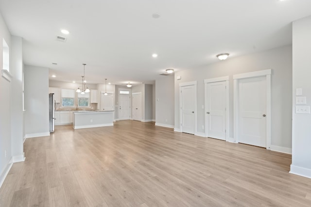 unfurnished living room with sink, light hardwood / wood-style flooring, and an inviting chandelier