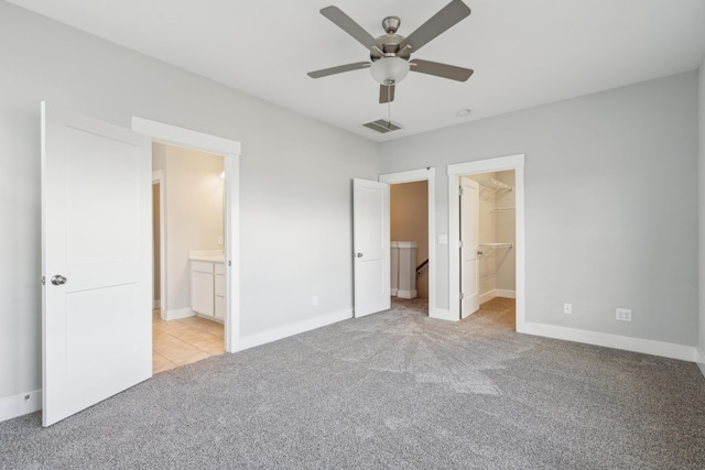 unfurnished bedroom with a walk in closet, ceiling fan, ensuite bath, and light carpet