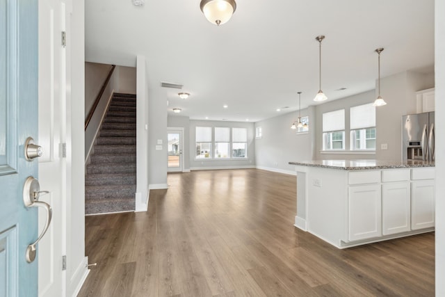 kitchen featuring white cabinets, stainless steel refrigerator with ice dispenser, hanging light fixtures, stone countertops, and dark hardwood / wood-style flooring