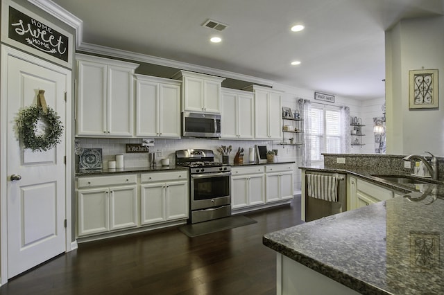 kitchen with stainless steel appliances, white cabinetry, sink, and dark stone counters