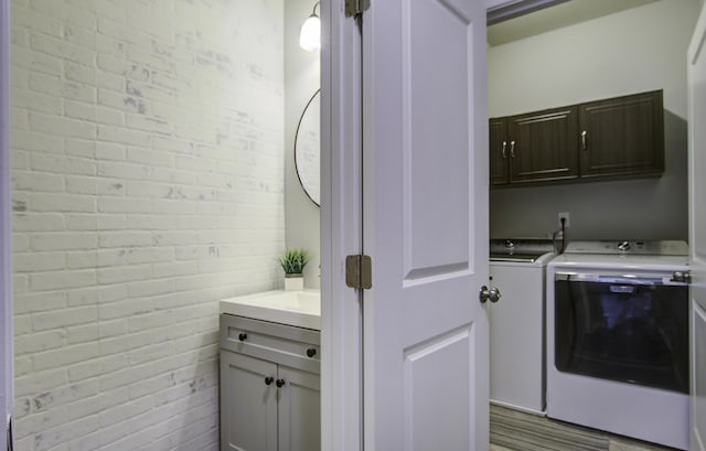 clothes washing area with cabinets, brick wall, and washing machine and clothes dryer