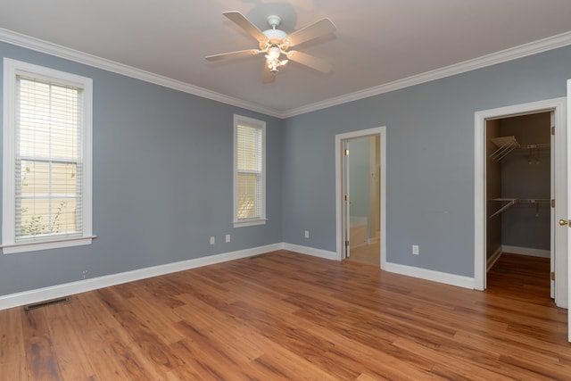 unfurnished bedroom featuring a walk in closet, multiple windows, light wood-type flooring, and crown molding