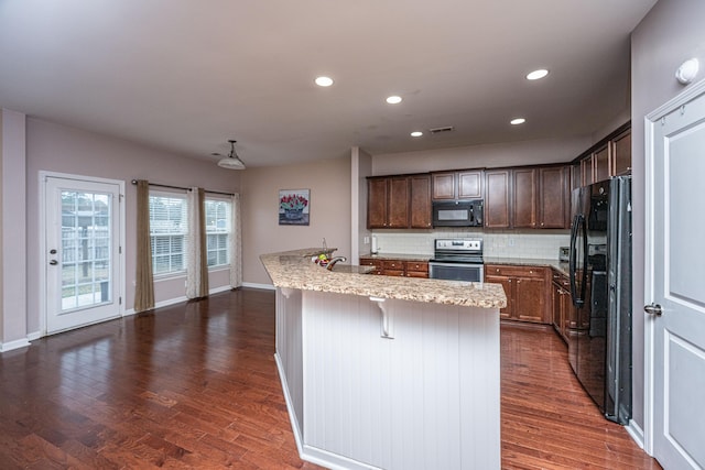 kitchen featuring dark wood-type flooring, sink, a breakfast bar area, a kitchen island with sink, and black appliances